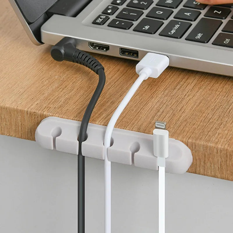 Scalloped Design Silicone Cable Organizer in white used at edge of table iwht cables and a loptop